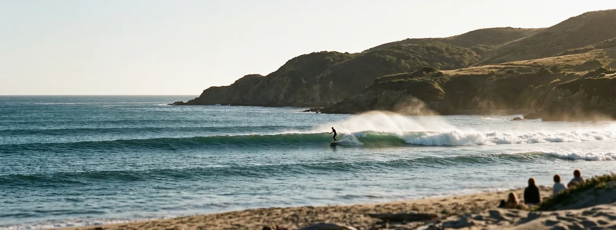 Distant surfer riding across a clean shoulder-high wave at a California point break in golden light