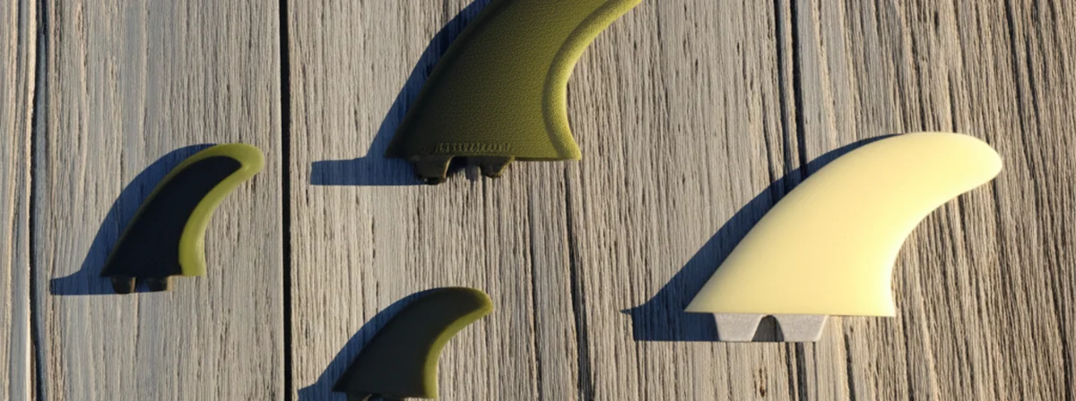 Surfboard fins laid flat on weathered wooden deck in warm natural light, showing different fin sizes from above