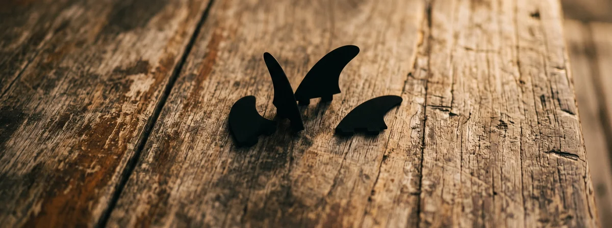 Overhead flat lay of surfboard fins on a weathered wood deck in warm natural daylight