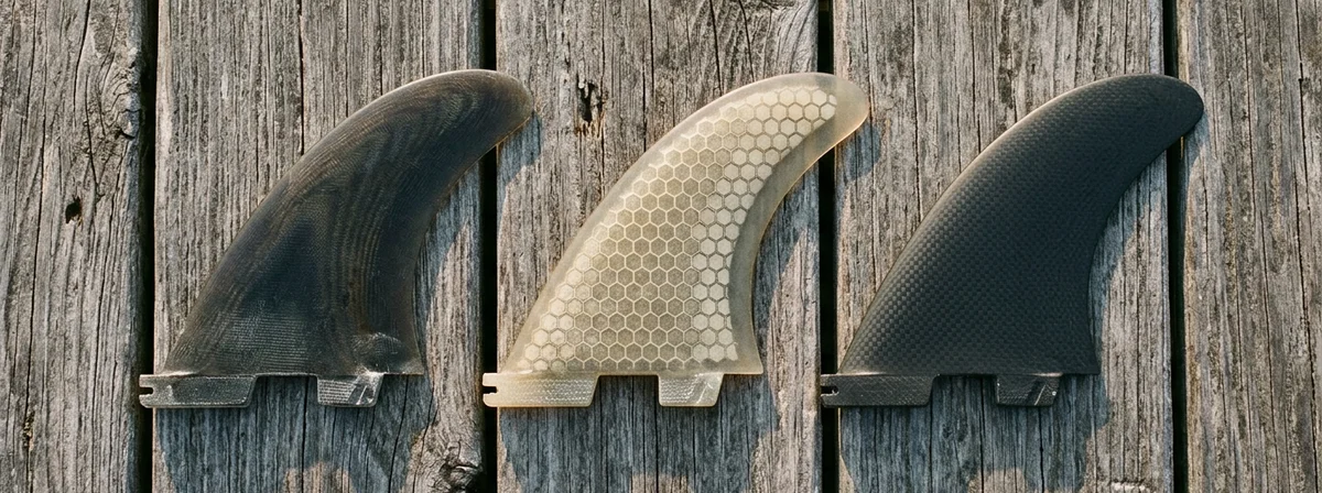 Surfboard fins laid on weathered wood deck in natural light showing different fin constructions