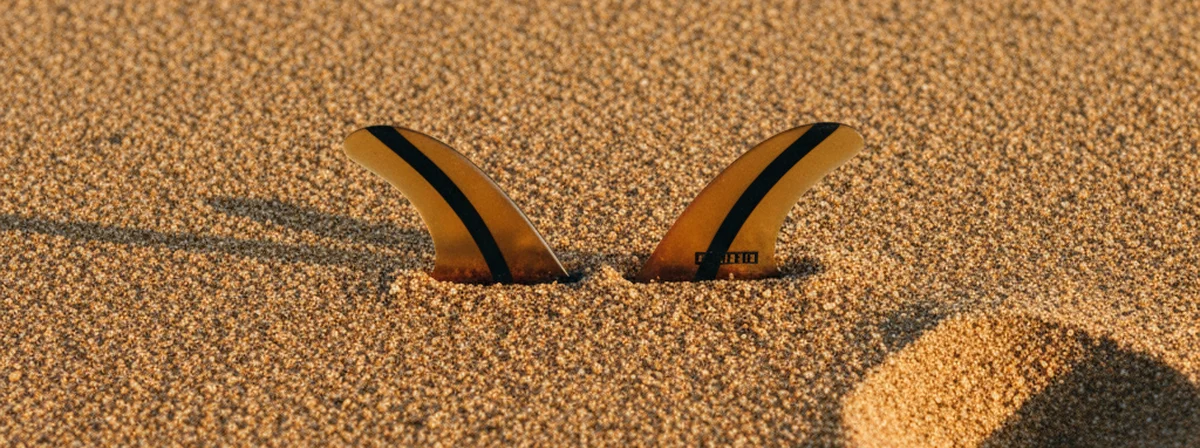 Twin keel fins laid flat on beach sand at golden hour with soft shadows
