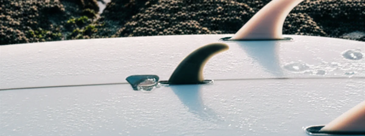 Small nubster trailer fin next to standard quad fins on a wet surfboard tail showing five-fin box configuration