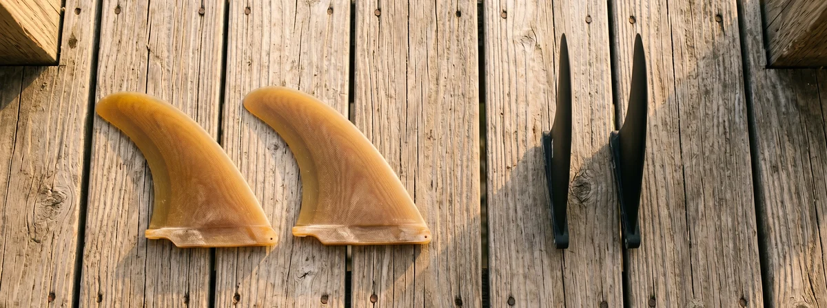 Two pairs of twin fins laid out on a weathered wood deck, classic fish keels next to modern upright twin templates in natural light.