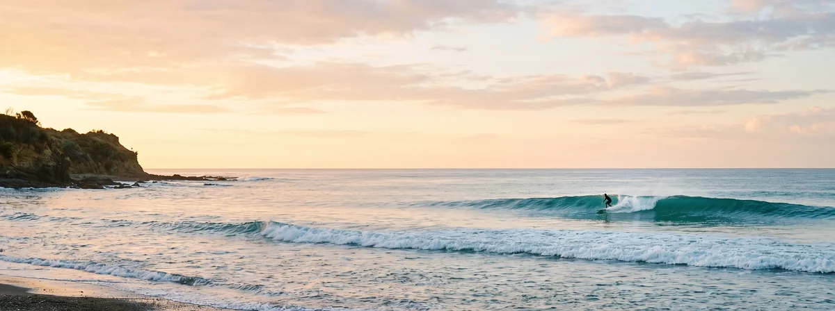 Distant surfer riding a clean wave at dawn, fins cutting a visible wake behind the board